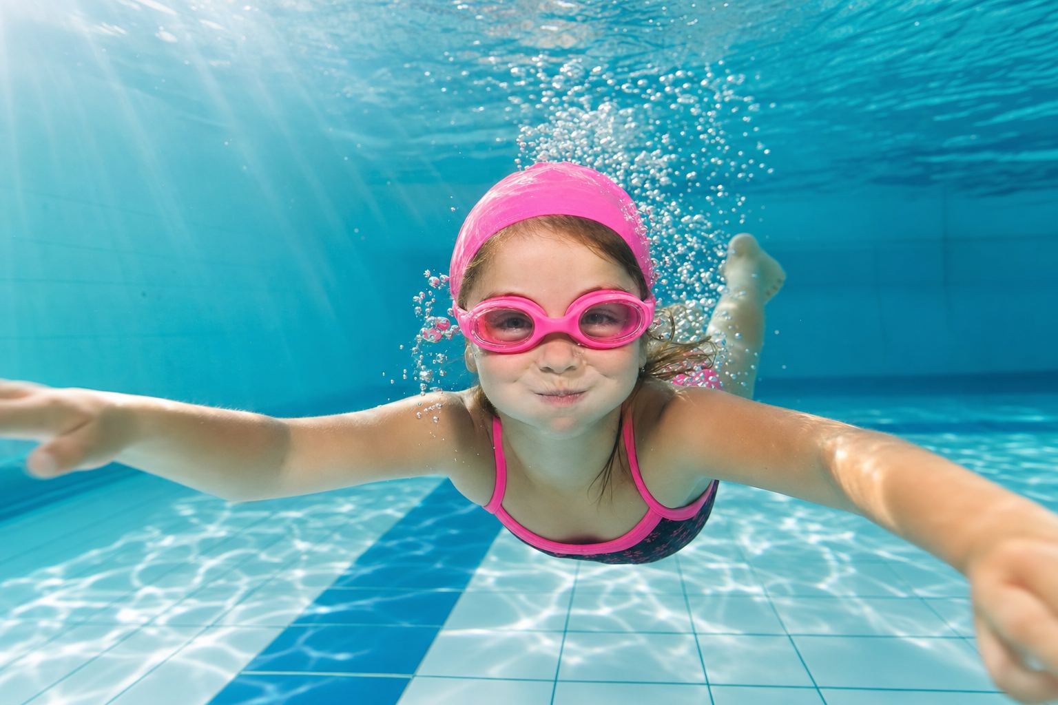 Mädchen mit Schwimmbrille taucht lachend durch das türkisblaue Wasser